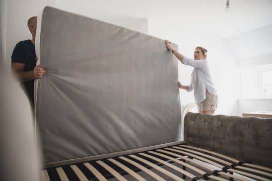 Photo of a couple flipping a gray mattress, woman is wearing a striped blouse. man wearing black shirt.