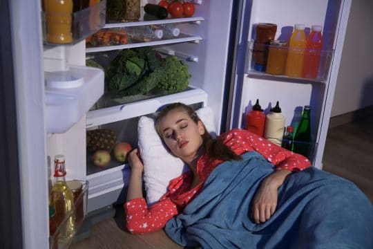 Woman sleeping in refrigerator blue blanket red shirt fruits and vegetables