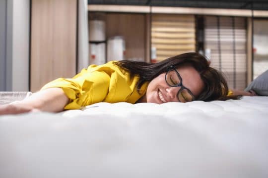 Buying a mattress. A beautiful girl is testing a new mattress before buying. Portrait of a satisfied brunette lying on a new bed. The concept of Healthy sleep