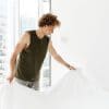Man making the bed white bedding tank top curly hair