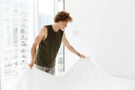 Man making the bed white bedding tank top curly hair